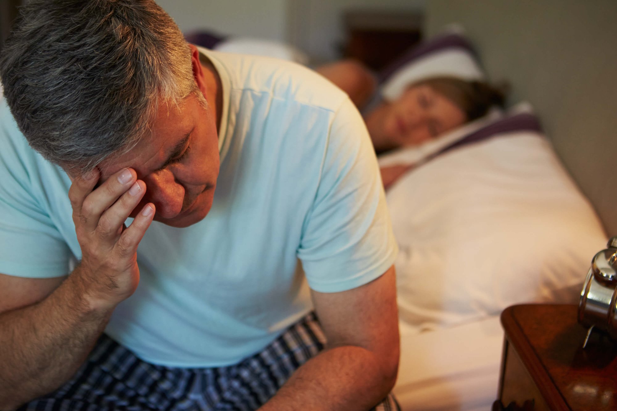 Man holding his forehead while sitting on the edge of his bed
